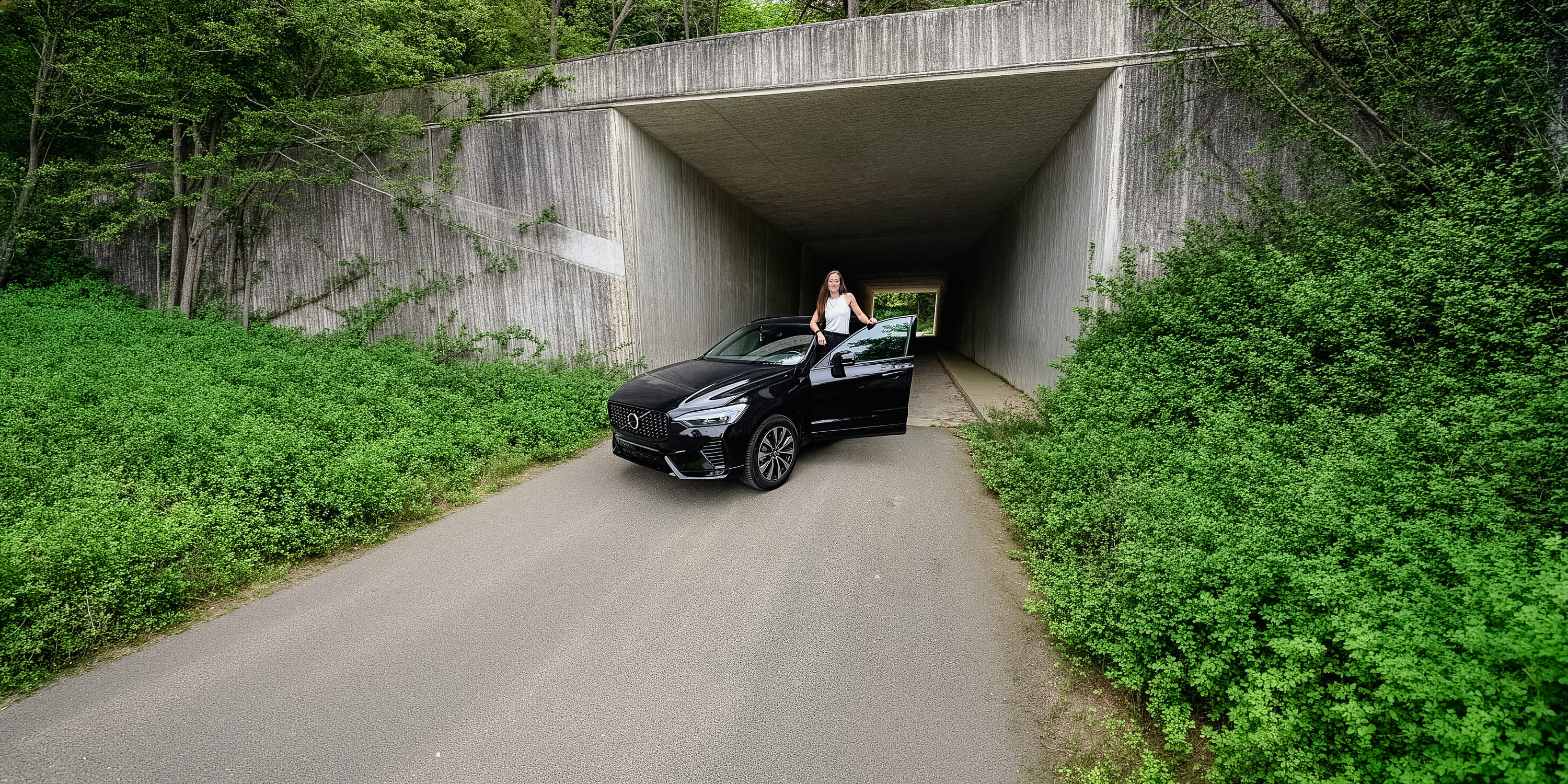 Kim Irmgartz steht vor einem Volvo‑Auto. Sie posiert vor dem Fahrzeug, das im Vordergrund gut sichtbar ist, während der Hintergrund eine klare Außenaufnahme zeigt.